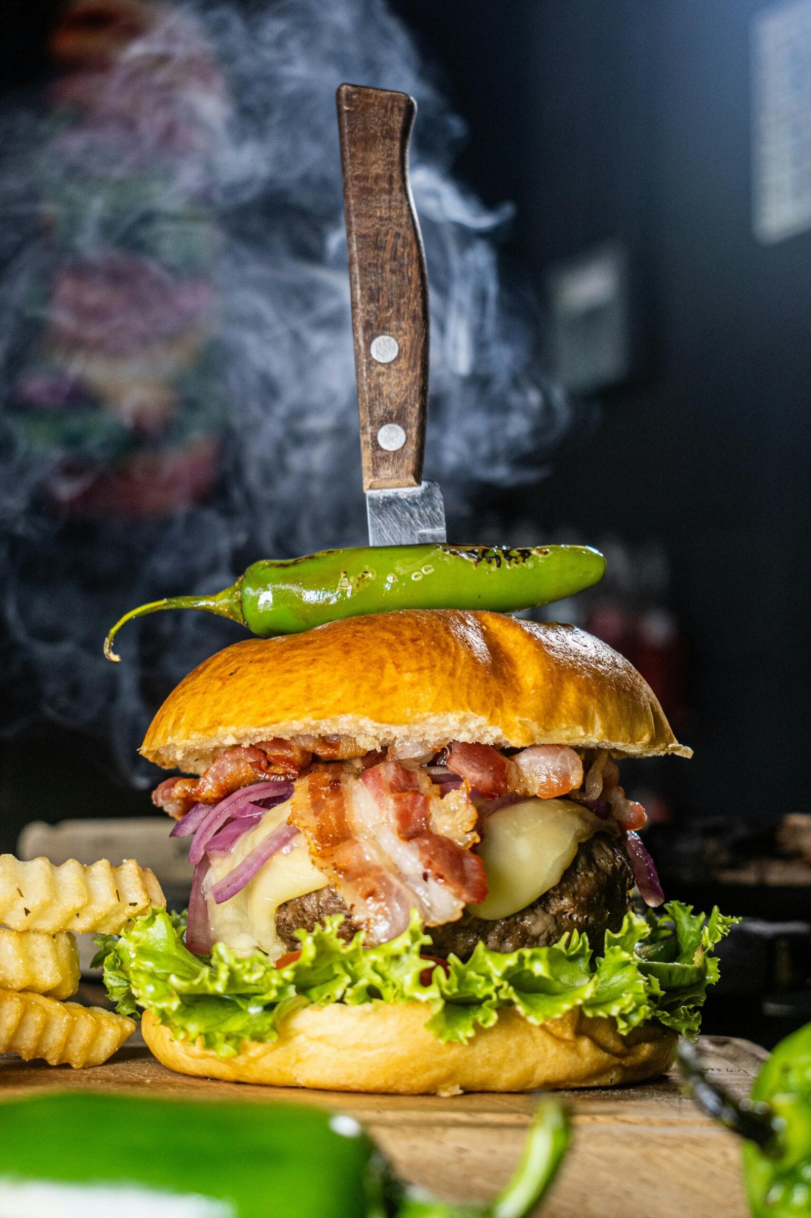 Sizzling bacon cheeseburger with jalapeño and knife, perfect for culinary delights.